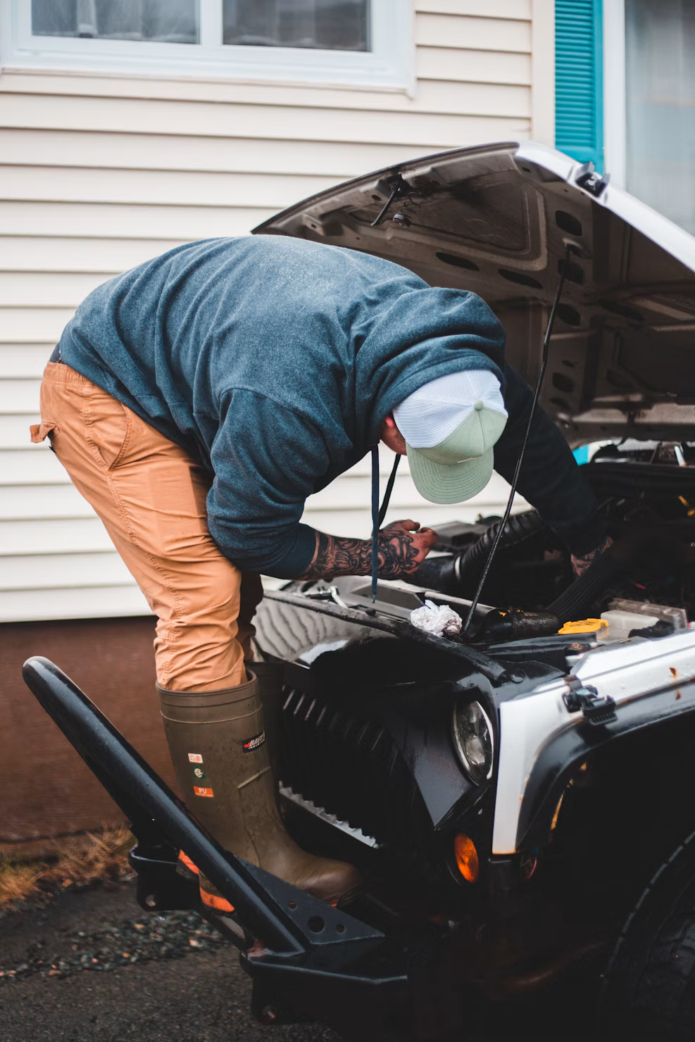 Mechanic working under the hood of a Jeep outside a home